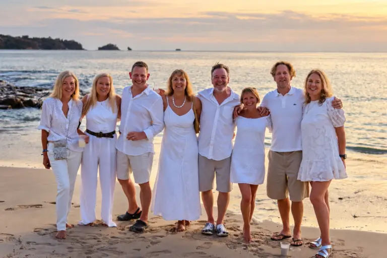 A group of friends dressed in white stand arm in arm on a Panama beach at sunset